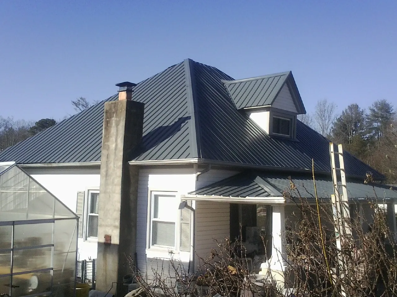 Dark blue standing seam metal roof on a white farmhouse with dormer — Slate & Tile Roof Repair by Roofing Brothers in Watkins