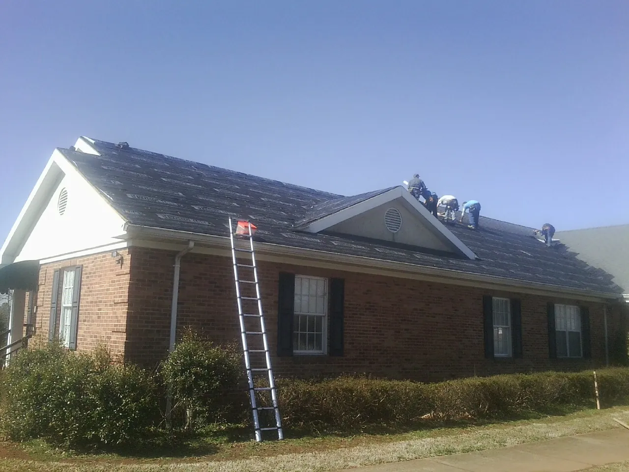 Crew tearing shingles off a brick ranch roof with a ladder set — Emergency Roof Repair work by our crew in Watkins