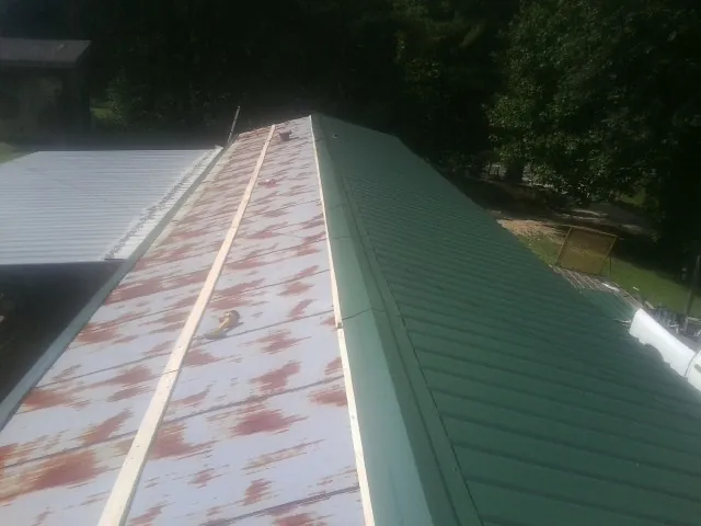 Old rusted panels beside newly installed green metal roofing — Wind Damage Roof Repair by Roofing Brothers in Watkins