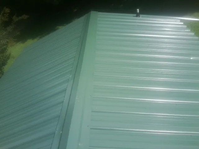 New green metal panels meeting at the ridge of a roof — Flat Roof Repair work by our crew in Watkins