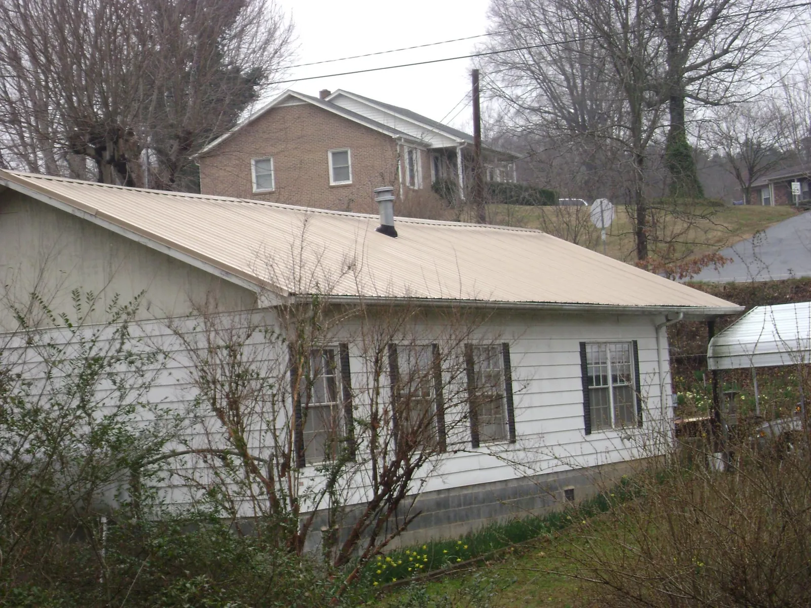 Tan metal roof on a white sided house set into a hillside — Commercial Roofing by Roofing Brothers in Watkins